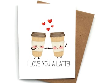 May include: A white card with two cartoon coffee cups holding hands. The cups have happy faces and red hearts are floating above them. The text on the card reads "I love you a latte!"