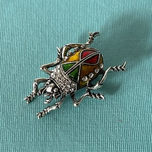 May include: A silver beetle brooch with red, yellow, and green enamel and clear rhinestones.