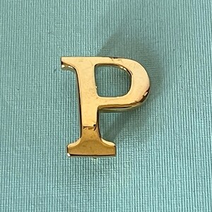May include: A gold-colored letter "P" against a light blue background. The letter is in a serif font and appears to be made of metal. The background has a textured appearance.