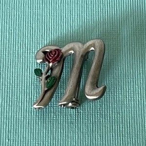 May include: Silver letter M charm with a red rose and green leaves.