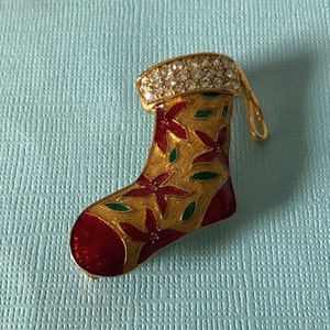 Puede incluir: Pin de Navidad de color dorado en forma de calcetín con esmalte rojo y verde y pedrería transparente.