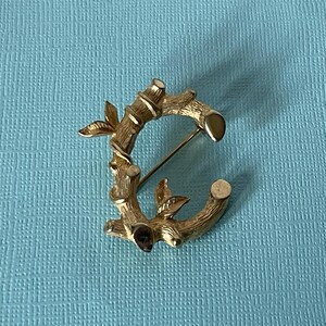 May include: Gold-toned brooch shaped like the letter C, with a design resembling bamboo branches and leaves.