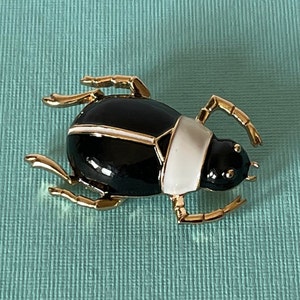 May include: A gold-tone beetle brooch with black and white enamel. The beetle has a detailed design with gold accents.