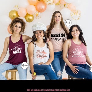 K&ouml;nnte beinhalten: Vier Frauen tragen Tanktops mit verschiedenen Designs zum Thema Western. Die Tanktops sind in den Farben Weinrot, Wei&szlig;, Pfirsich und Weinrot. Der Text auf den Tanktops lautet "Cowgirl Gang", "My Last Rodeo", "Getting Rowdy" und "Whiskey Bent & Veil Bound".