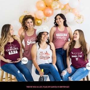 K&ouml;nnte beinhalten: F&uuml;nf Frauen tragen Tanktops mit verschiedenen Spr&uuml;chen zum Thema Western. Die Spr&uuml;che auf den Tanktops lauten "Cowgirl Gang", "Let's Go Girls", "My Last Rodeo", "Getting Rowdy" und "Howdy Y'all".