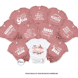 K&ouml;nnte beinhalten: Ein Set aus zehn pinkfarbenen und wei&szlig;en T-Shirts mit verschiedenen Designs und Texten zum Thema Western, darunter "Let's Go Girls", "Whiskey Bent & Veil Bound", "Let's Get Nasty", "Getting Rowdy", "These Boots Were Made For Walkin' Down The Aisle", "Howdy Let's Get Rowdy", "Wild West", "Last Hoe Down", "Cowgirl Gang" und "My Last Rodeo".