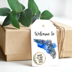 May include: White gift tag with a blue watercolor outline of the state of Florida. The text "Welcome to Florida" is written in black cursive font. A circle with the text "Room to add your logo" is in the bottom left corner.