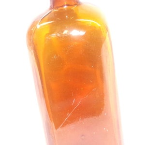 May include: A brown glass bottle with a wide mouth and a rounded bottom. The bottle is empty and has a slight tilt.