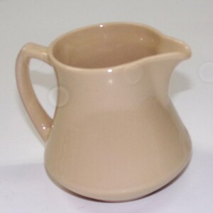 May include: A beige ceramic pitcher with a curved body, a handle, and a spout. The pitcher has a smooth, glossy finish and is designed for pouring liquids. The neutral color makes it suitable for various kitchen styles.
