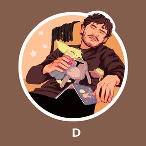 May include: A man with brown hair and a beard is sleeping in a chair. He is holding a green and yellow creature and a gray and white creature. He is also holding a book that says "Eat Sleep Create".
