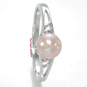 May include: A silver ring featuring a single round, pale pink pearl set in a polished metal band with an openwork, lattice-style design on the shoulders. The text The Pearl Jewelers is printed vertically along the side of the ring band.