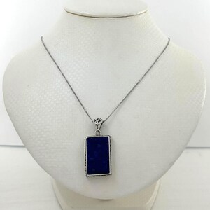 May include: A silver necklace with a rectangular, deep blue pendant. The pendant is framed in silver and hangs from a delicate chain. The necklace is displayed on a white mannequin bust.