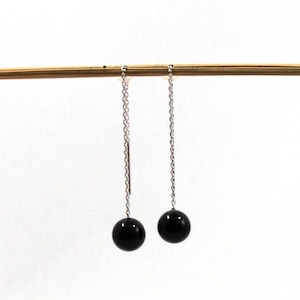 Può includere: Un paio di orecchini pendenti con perle nere e catene d'argento.