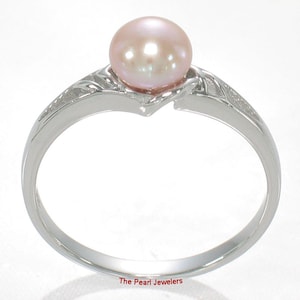 May include: A silver-toned ring featuring a single round, pale pink pearl set at the center. The band has a polished finish with textured, leaf-like detailing on the shoulders leading up to the pearl setting. The text The Pearl Jewelers is visible.