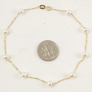 May include: A delicate gold necklace featuring small, white pearls evenly spaced along a thin, twisted gold chain. The necklace is shown on a white surface, with a dime for size comparison. The clasp is visible.