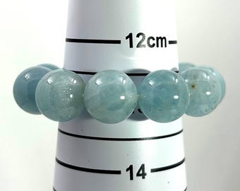 May include: A light blue aquamarine gemstone bracelet. The bracelet is composed of large, round beads. The beads are a translucent, pale blue color. The bracelet is displayed on a white measuring tool, with the 12 cm mark visible.