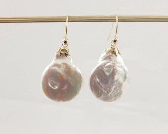 May include: A pair of gold-toned drop earrings featuring large, irregularly shaped, pearlescent white pearls. The earrings hang from gold-colored hooks and have decorative gold caps.