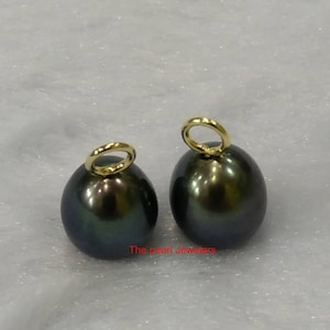 Op de afbeelding: Twee donkergroene ovale parels met gouden springringen. De parels zijn ongeveer 10 mm groot.