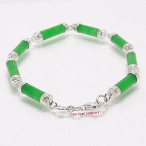 May include: A jade bracelet featuring cylindrical green jade beads connected by silver-toned metal links. The bracelet has a clasp closure and is displayed on a white surface. The Pearl Jewelers is printed on the bottom right.