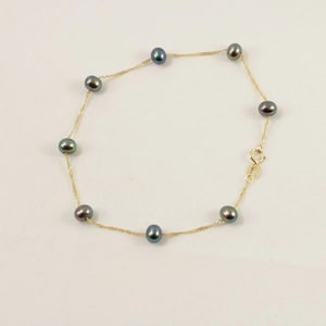 May include: A delicate gold chain bracelet featuring eight dark gray pearls. The pearls are evenly spaced along the chain, which fastens with a small clasp. The bracelet is displayed against a white background.