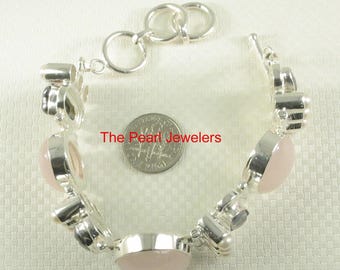 Puede incluir: Un brazalete de plata con piedras de cuarzo rosa ovaladas y redondas. El brazalete tiene un cierre de palanca y está sobre una superficie clara. El texto "The Pearl Jewelers" es visible.