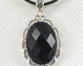 Peut inclure: Un collier pendentif en argent avec une grosse pierre précieuse ovale, facettée, bleu foncé, avec des inclusions scintillantes. La pierre précieuse est sertie dans un cadre argenté décoratif et est suspendue à un cordon noir.