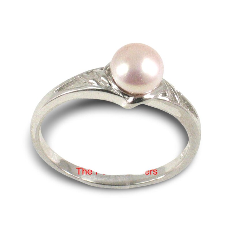 May include: A silver-toned ring featuring a single, smooth, pale pink pearl set at the top. The band has a polished metallic finish with subtle, etched, angular detailing along the sides. The text "The" and "ers" is visible on the inner band.