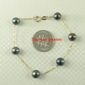 May include: A delicate gold chain bracelet featuring seven dark gray pearls. The pearls are evenly spaced along the chain, which is secured with a small clasp. The text "The Pearl Jewelers" is visible on a dime next to the bracelet.