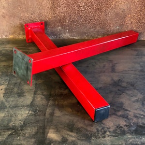 May include: Two red metal table legs with square bases. The legs are joined together in an X shape. The bases have a black rubber cap.