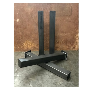 May include: Three black metal table legs with a square cross-section. The legs are stacked on top of each other and have a welded plate at the bottom. The legs are labeled "#500B/1".