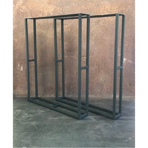 May include: Two black metal display stands with a rectangular frame and a shelf. The stands are positioned side-by-side on a concrete floor.