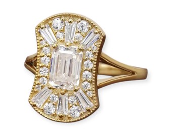May include: A gold-toned ring featuring a rectangular, emerald-cut center stone surrounded by smaller, baguette-cut and round diamonds. The ring has a decorative, Art Deco-inspired design with a split shank band.