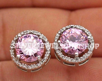 May include: A pair of silver earrings with a pink gemstone surrounded by a halo of smaller white gemstones.