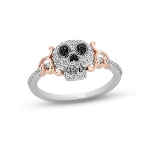 May include: A silver and rose gold ring with a skull design. The skull is made of white diamonds and has black diamond eyes. The ring is set with small diamonds around the band.
