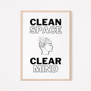 May include: A framed print with the words "CLEAN SPACE" above "CLEAR MIND" in bold, black letters. A black and white illustration of a person's profile with a lightbulb in their head is centered between the text. The frame is a light wood color.