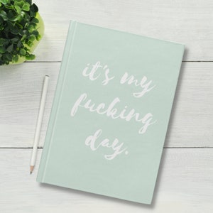 Può includere: Un diario verde chiaro con il testo "it's my fucking day." scritto in corsivo bianco.