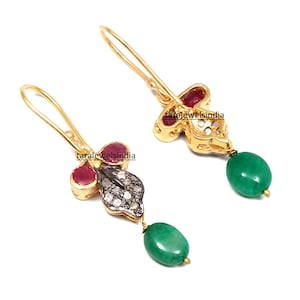 Op de afbeelding: Gouden oorbellen met een bloemmotief met rode robijnstenen en witte diamanten. De oorbellen hebben een groene edelsteendruppel.