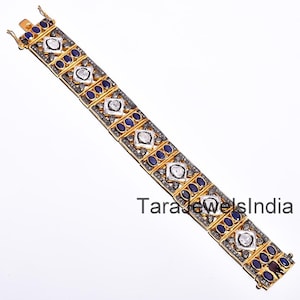 May include: A gold-toned bracelet with alternating square and oval-shaped gemstones. The square stones are white, and the oval stones are dark blue. The bracelet has a clasp closure and is set against a white background.