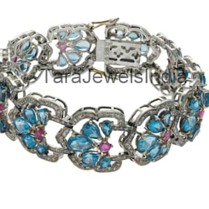 May include: A silver bracelet with a floral design featuring blue topaz and pink ruby gemstones. The bracelet has a clasp closure.