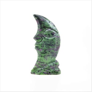 May include: Green and purple crescent moon carving made from a green gemstone. The moon has a face carved into it.