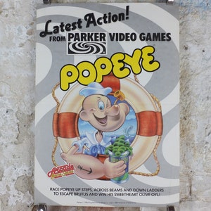 May include: A vintage Popeye arcade game poster. The poster features Popeye the Sailor holding a can of spinach, with a life preserver and the words "Popeye" in large yellow letters. The poster also includes the text "Latest Action!" and "Arcade Game Series."