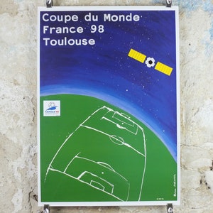 May include: A poster for the 1998 FIFA World Cup in Toulouse, France. The artwork features a green soccer field, a satellite with a soccer ball, and the text "Coupe du Monde France 98 Toulouse" against a blue and starry background.
