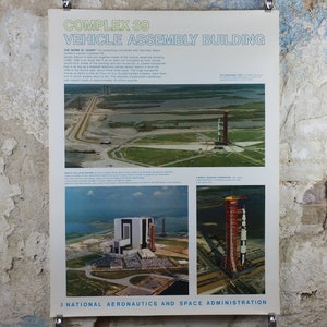 May include: Vintage poster titled "Complex 39 Vehicle Assembly Building" with images of the Apollo program. The poster features aerial views of the launch site, assembly building, and a rocket on a mobile launcher. Text includes details about the program.