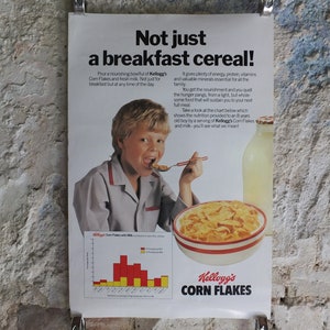 Op de afbeelding: Vintage Kellogg's Corn Flakes-advertentie. Een jongen eet ontbijtgranen uit een kom. De poster bevat de tekst "Not just a breakfast cereal!" en een voedingswaardetabel. Een melkfles is ook zichtbaar.