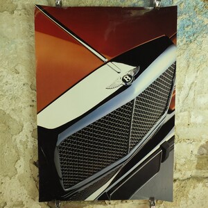 May include: A detailed shot of a Bentley car's front, highlighting the chrome grille and emblem. The hood features orange, white, and black panels. The image is displayed on a textured wall, with the car's design taking centre stage.