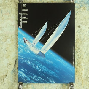Könnte beinhalten: Poster für die Olympischen Spiele 1992 in Barcelona, mit zwei Segelbooten, die vor einem blauen und schwarzen Hintergrund segeln. Das Poster enthält die olympischen Ringe und Text in mehreren Sprachen.