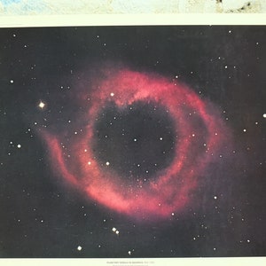 May include: A print depicting a planetary nebula in space, with a striking red and pink ring set against a black backdrop sprinkled with white stars. The nebula is circular, with a dark central area. The print is on cream-coloured paper.