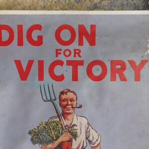 Puede incluir: Cartel vintage con el texto "DIG ON FOR VICTORY" en rojo. La imagen muestra a un hombre sonriente con una pipa, sosteniendo un horca y verduras. El fondo es azul claro, con pinzas met&aacute;licas.