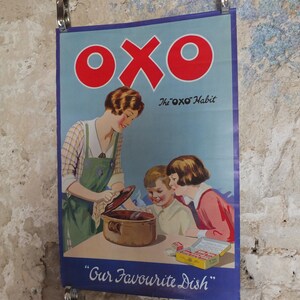 Può includere: Poster pubblicitario vintage Oxo con una donna e due bambini attorno a una pentola. Il poster ha un bordo blu e il logo Oxo in rosso. Il testo include "The Oxo Habit" e "Our Favourite Dish".