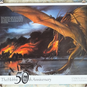 Puede incluir: Un póster del 50 aniversario de El Hobbit. Un dragón con alas naranjas y boca de fuego vuela sobre un pueblo en llamas. El texto dice: "Flames unquenchable sprang into the night..." y "Unwin Hyman, Unwin Paperbacks."